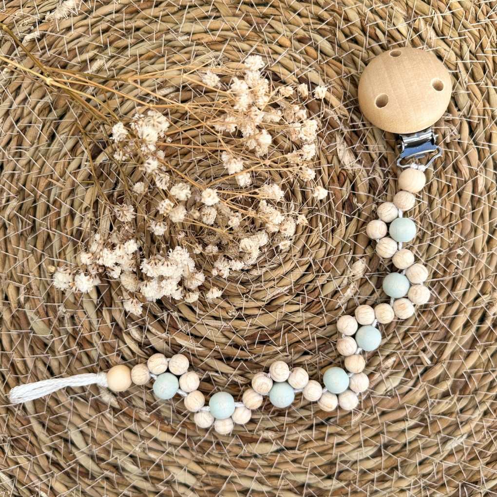 Schnullerketten-Bastelset „Twist“ mit naturbelassenen Holzperlen, pastellblauen Akzenten und Holzclip auf Bastunterlage – ideales DIY-Set zum Selbermachen einer individuellen Schnullerkette.